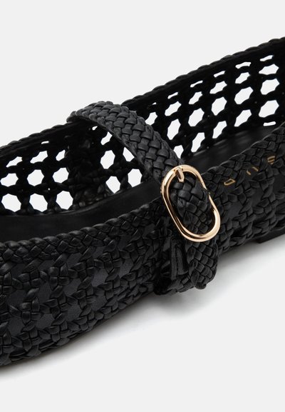 Chaussure plate en cuir tressé noir avec une bride à boucle dorée et un design à treillis ouvert sur les côtés.