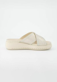 Beige schuiflippers met gekruiste banden, gemaakt van zacht materiaal. Textuur rubberen zool, dikke basis, met stiksel details op de banden.