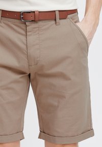 Könnyű anyagból készült, rolled cuffs-szal ellátott khaki sort, oldalsó zsebekkel és egy barna bőr övvel, ezüst csattal.