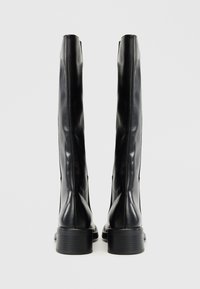 Bottes noires montantes en cuir lisse avec un bout rond et un petit talon block. Présente un design minimaliste avec des lignes épurées.