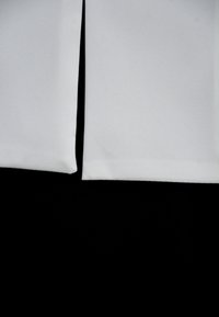 Biała tkanina o gładkiej fakturze, starannie złożona, wyrównana na czarnym tle. Dwie wyraźne białe sekcje z czystymi krawędziami.