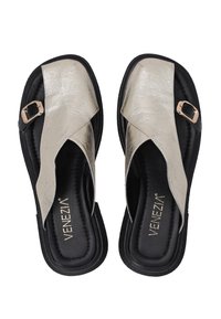 Goldene Metallic-Slipper mit einem Kreuzriemendesign, ausgestattet mit einer schwarzen Sohle und einem dekorativen Schnallenakzent. Flacher und strukturierter Fußbett.