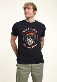 Camiseta negra de manga corta con un gráfico central de una calavera con un casco y llamas, rodeada de texto rojo y amarillo.