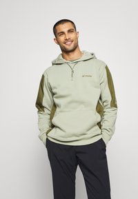 Light green hoodie with darker green sleeves, featuring a quarter zip and logo on the chest. Constructed from soft fabric, designed for comfort.