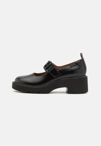 Black patent leather Mary Jane shoe with a square toe, matching strap and buckle, and a chunky platform heel with treaded rubber sole.