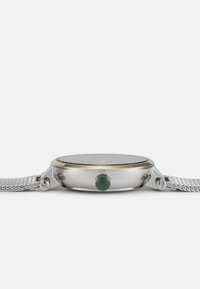 Reloj de metal plateado con una esfera negra, bisel de tono dorado y acento de gema verde en la corona, con una correa de malla de plata tejida.