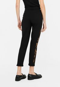 Pantaloni della tuta neri a vestibilità slim, con una striscia a stampa leopardata. Finiture arrotolate e una cintura comoda. Mocassini neri indossati per contrasto.