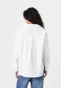 Witte, langmouwige shirt met een rugplooi, een klassieke kraag en knoopmanchetten. Gecombineerd met lichtblauwe denim jeans.