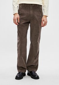 Pantaloni din catifea subțire maro cu croială dreaptă, cu textură în dungi, și buzunare laterale, asortați cu pantofi din piele negri, pe un fundal simplu.