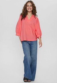 Blusa di seta corallo con scollatura a V, maniche a palloncino, abbinata a jeans a vita alta a zampa d'elefante blu e tacchi aperti neri.