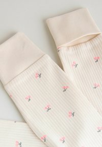 Pehmeä kermanvärinen ribbineulos, jossa pienet vaaleanpunaiset ja harmaat kirsikkakuviot sekä taitetut hihansuut vaalealla taustalla.