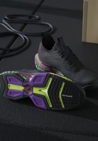 Paire de chaussures de sport noires avec des semelles violettes, vertes et multicolores, une chaussure allongée sur le côté montrant le logo Continental sur la semelle.