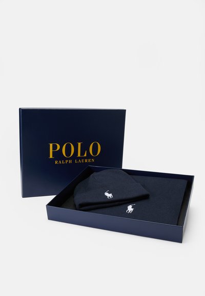 Caixa de presente azul marinho contendo um gorro de malha e um cachecol, ambos com um logo branco. A tampa da caixa apresenta "POLO RALPH LAUREN" em texto dourado.