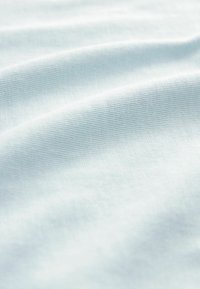 Ljusblått texturerat tyg med ett subtilt mönster, som har mjuka, släta ytor och varsamma veck, vilket visar på ett lätt material.