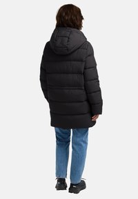 Giacca a vento nera con cappuccio, caratterizzata da un design trapuntato e polsini elasticizzati, abbinata a jeans blu a gamba dritta e calzature nere.