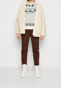 Off-white fleecetröja, mönstrad stickad tröja i vitt och grönt, bruna byxor och vita snörade chunky stövlar. Enkel och avslappnad passform.