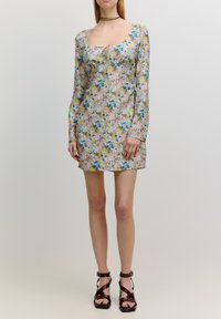 Mini-jurk met bloemenprint en lange mouwen in pastelkleuren, met een vierkante halslijn en trekkoorddetail. Gecombineerd met bruin leren hakken met banden.