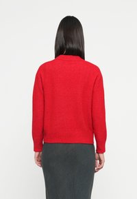 Red knitted sweater with a rounded neckline and long sleeves. Smooth texture with a fitted waist. Back view shows solid color design.