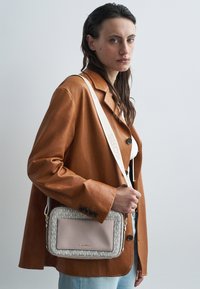 Bolso bandolera de Michael Kors con estampado de monograma en crema y beige, frente de cuero suave de color rosa claro y correa ajustable con detalle del logotipo.