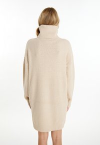 Rochie pulover oversized bej, cu guler înalt ribitat, model tricotat texturat, mâneci lungi și o tiv drept la lungimea mijlocului coapsei.