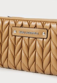 Brown leather bag with a quilted design featuring large, twisted patterns. Silver logo plate reads "KARL LAGERFELD." Smooth texture.