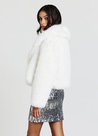 White faux fur cropped jacket with a hood, featuring long sleeves. Worn over a shimmering silver sequined mini skirt.