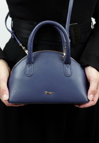 Navy leren handtas met een afgeronde bovenkant, korte handvatten, gouden hardware en een klein logo detail. Voorzien van een ritssluiting en een verstelbare schouderband.