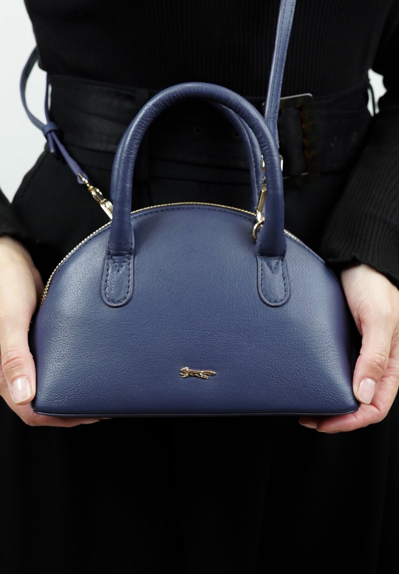 Navy leren handtas met een afgeronde bovenkant, korte handvatten, gouden hardware en een klein logo detail. Voorzien van een ritssluiting en een verstelbare schouderband.