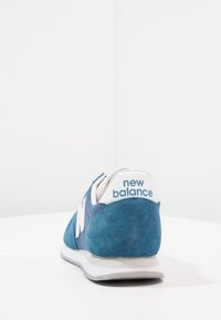 Modré semišové a síťované tenisky s bílými akcenty a šedou podrážkou. Na patě se nachází logo "new balance" a mají zaoblený design špičky.