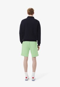 Sweatshirt marine avec col, associé à un short vert clair. Baskets blanches avec accents rouges et bleus, poignets côtelés sur le sweatshirt.