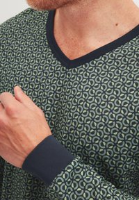 Langarmshirt in donkerblauw met een groen cirkelpatroon. Het heeft een V-hals en effen donkerblauwe manchetten. Zachte stoftextuur.