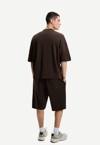 Hnedé oversized tričko a zodpovedajúce šortky vyrobené z mäkkej a priedušnej tkaniny. Šortky majú bočné vrecká a nenápadný detail loga na zadnej strane.