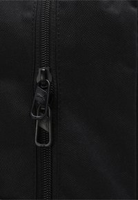 Juodas audinio kuprinė su lygiu užtrauktuku ir dviem traukimo juostelėmis bei subtiliu tekstūros raštu, pabrėžianti tvirtumą ir funkcionalų dizainą.