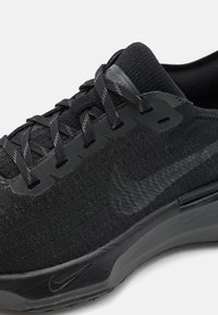 Scarpa sportiva nera con tomaia in maglia testurizzata, lacci piatti, occhielli sagomati e suola liscia e curvata con un discreto dettaglio del logo.