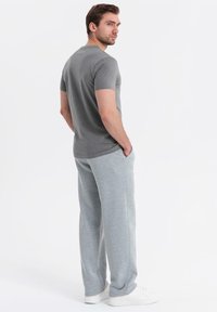 Maglietta grigia a maniche corte con scollatura rotonda, abbinata a pantaloni della tuta grigi chiari. L'outfit presenta una vestibilità comoda e una leggera texture.