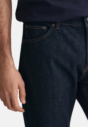Jeans en denim foncé avec une coupe slim, des coutures orange, un design classique à cinq poches et une quincaillerie en métal au niveau de la taille.