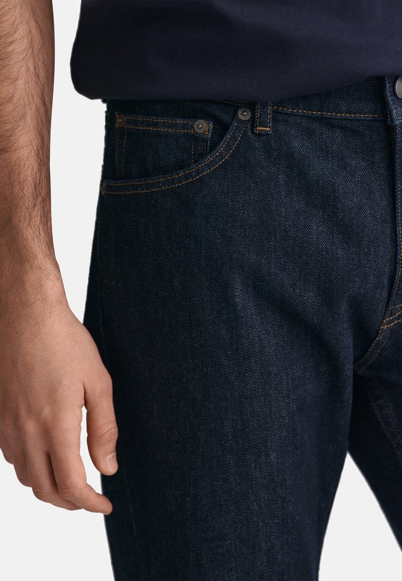 Jeans in denim scuro con vestibilità slim, cuciture arancioni, design classico a cinque tasche e chiusura con bottone metallico in vita.