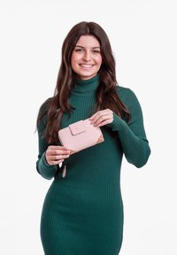 Pink wallet with a patterned accent, featuring a front clasp and a zippered compartment, held by a person in a green ribbed dress.