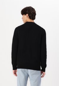 Maglione a coste nere con maniche lunghe, collo rotondo e orlo dritto. Il tessuto sembra morbido con una lieve texture.