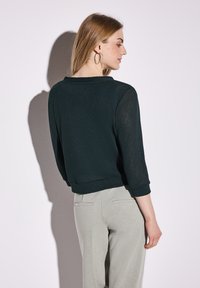 Mörkgrön, texturerad pullovertröja med trekvartsärmar, bärs med ljusgrå byxor; har en enkel, rund halsringning och ribbade ärmslut.