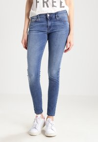 Blå denim skinny jeans med hög midja, subtil slitning och en slät textur, i kombination med vita sneakers.