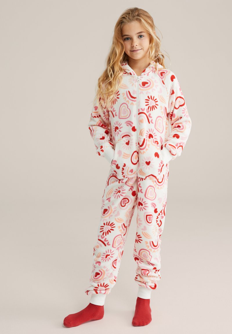 Mameluco con capucha de material de forro polar, con un patrón de corazones y estrellas en rojo y rosa sobre un fondo crema. Cremallera frontal y puños blancos.
