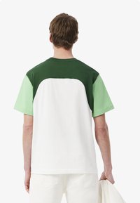 Camiseta de manga corta con bloques de color que presenta un cuerpo blanco, espalda verde y mangas verde menta. Fabricada en algodón suave con cuello redondo.