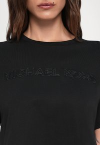 Juodas medvilnės marškinėliai su apvaliu iškirpimu ir tekstūruotu siuvinėjimu "MICHAEL KORS" krūtinės srityje.