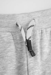 Szare bawełniane dresy z elastycznym pasem, z czarno-białym sznurkiem wciąganym z plastikowym końcem oraz kieszeniami bocznymi.