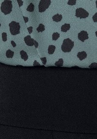 Groene stof met zwart dierenprint boven een zwarte, gestructureerde sectie, met een zachte, licht glanzende afwerking en een gelaagd ontwerp.