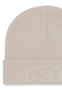Gebreide beige beanie met een omgeslagen rand en een reliëftekst "HUEY" aan de voorkant. Het materiaal heeft een zachte, gestructureerde uitstraling.