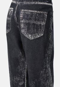 Jeans de mezclilla negra con una textura desgastada y rasgada. Incluye dos bolsillos traseros con solapas punteadas y detalles de costura visibles.