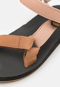 Cinghie in tessuto marrone e beige con suola in gomma nera texturizzata. Presenta un'etichetta con logo sulla cinghia e un design tessuto sulla soletta.