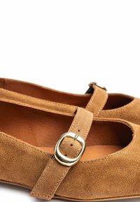 Zapatos Mary Jane de ante color canela con punta redonda, con una correa estrecha y hebilla metálica dorada. Textura suave y detalles mínimos de costura.